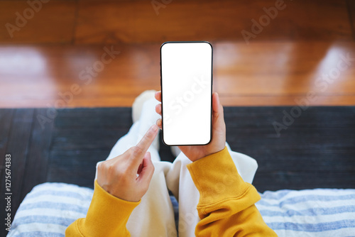 Top view mockup image of a woman holding mobile phone with blank desktop screen while sitting in bed room at home