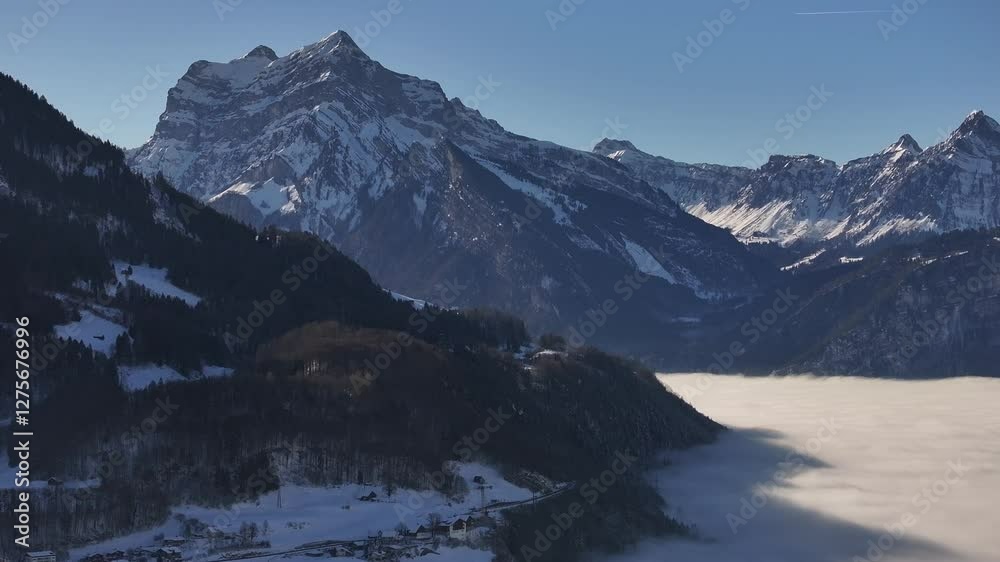 Aerial view in Glarus, Switzerland. Stunning landscape featuring a sea of fog covering the lake, with majestic alpine peaks towering under clear skies.