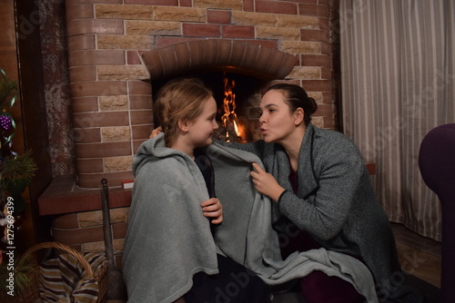A young parent and child enjoy cozy leisure time by the fireplace, embracing the warmth and comfort of winter time indoors. Hygge concept. Family bonds and shares precious moments together t home