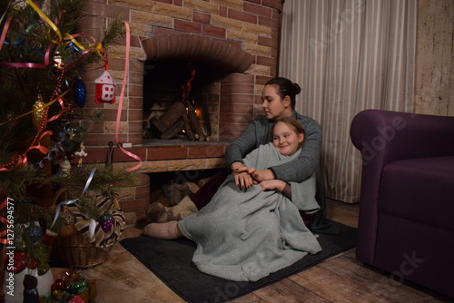 A young parent and child enjoy cozy leisure time by the fireplace, embracing the warmth and comfort of winter time indoors. Hygge concept. Family bonds and shares precious moments together t home