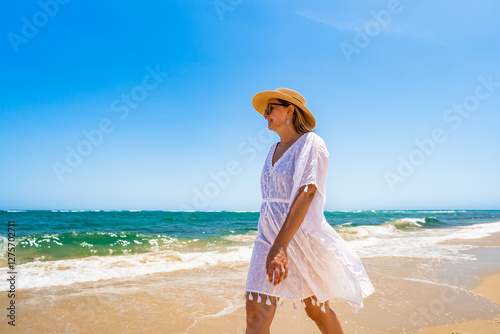 Beautiful mature woman walking on sunny sandy paradise beach on Armona island in Portugal. Travel destination - Armona beach. Side view photo