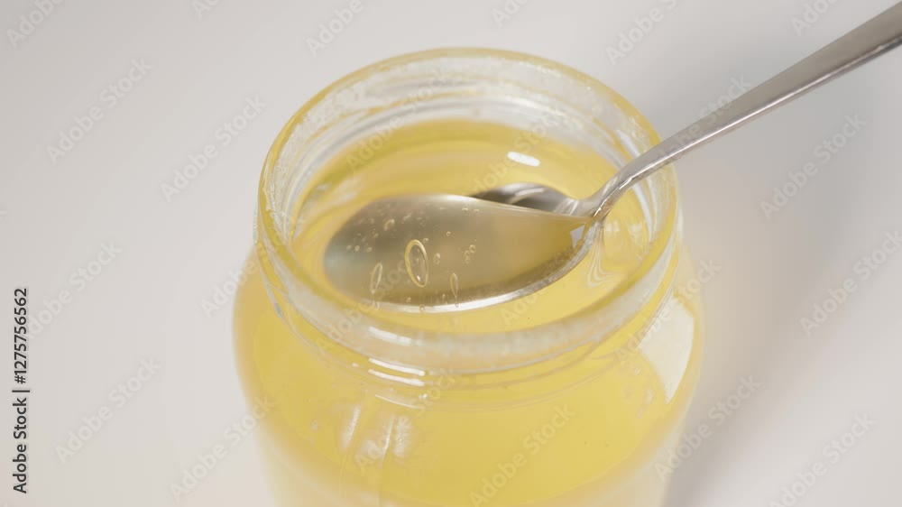 A bright and detailed photograph showcasing a jar of honey with a spoon submerged inside, highlighting the golden, translucent texture of the honey. A bright and detailed photograph showcasing a jar of honey with a spoon submerged inside, highlighting the golden, translucent texture of the honey.