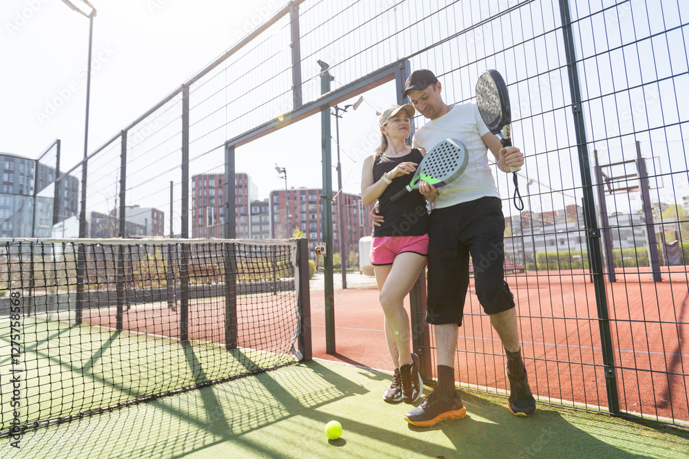 Φωτογραφία Cheerful athletic couple laughing during padel tennis match on outdoor court