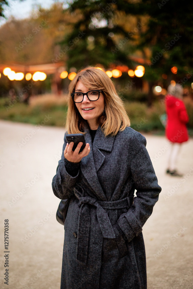 Fototapeta premium Attractive mid aged woman walking on the street and using her smartphone
