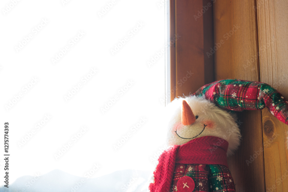 pupazzo di neve di stoffa, che sorride, decorato in tema natalizio, di fianco ad una finestra