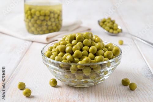 Canned organic green peas in a glass bowl. Wet marinated sweet peas in a bowl spoon and glass jar on a white woodem table. Vegetable protein dietary fiber concept. photo