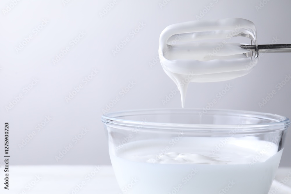 Hand mixer with whisks and bowl of whipped cream on white table, closeup. Space for text Hand mixer with whisks and bowl of whipped cream on white table, closeup. Space for text