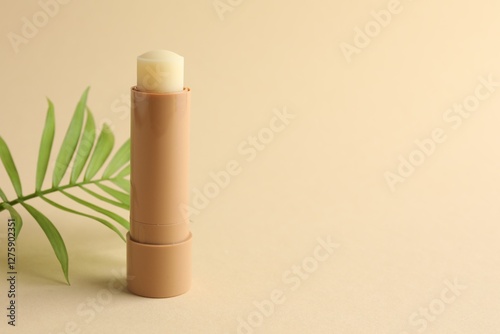 Lip balm and leaves on beige background, closeup. Space for text
