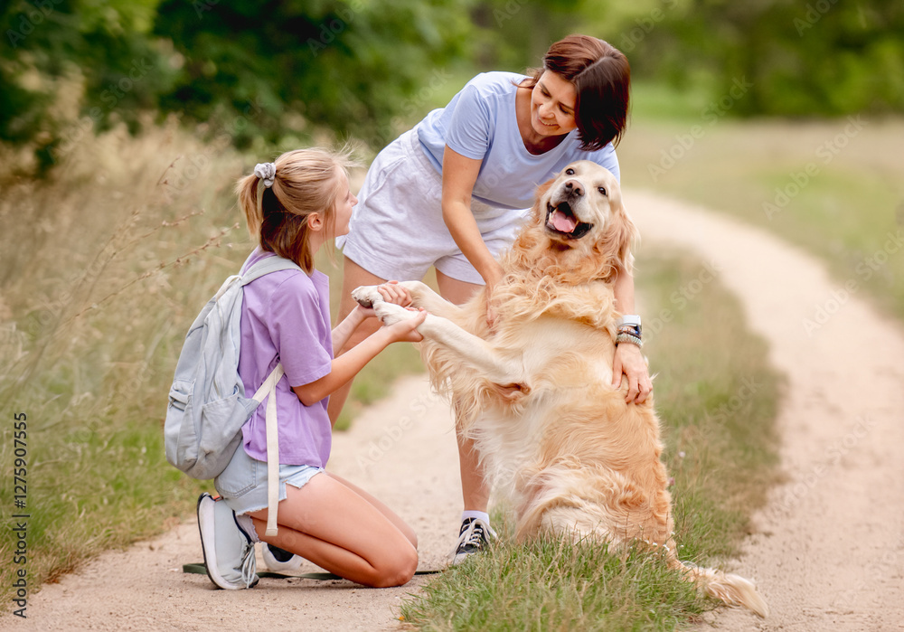 Daughter And Mother Teaching Golden Retriever Dog To Give Its Paw Happily During The Summer Daughter And Mother Teaching Golden Retriever Dog To Give Its Paw Happily During The Summer