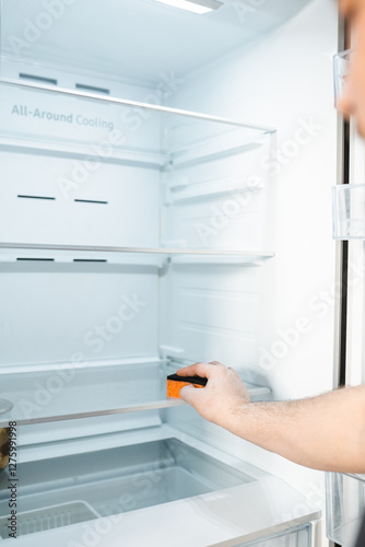 Man cleans up  a refrigerator shelf. Kitchen chores. Man cleaning fridge with sponge.