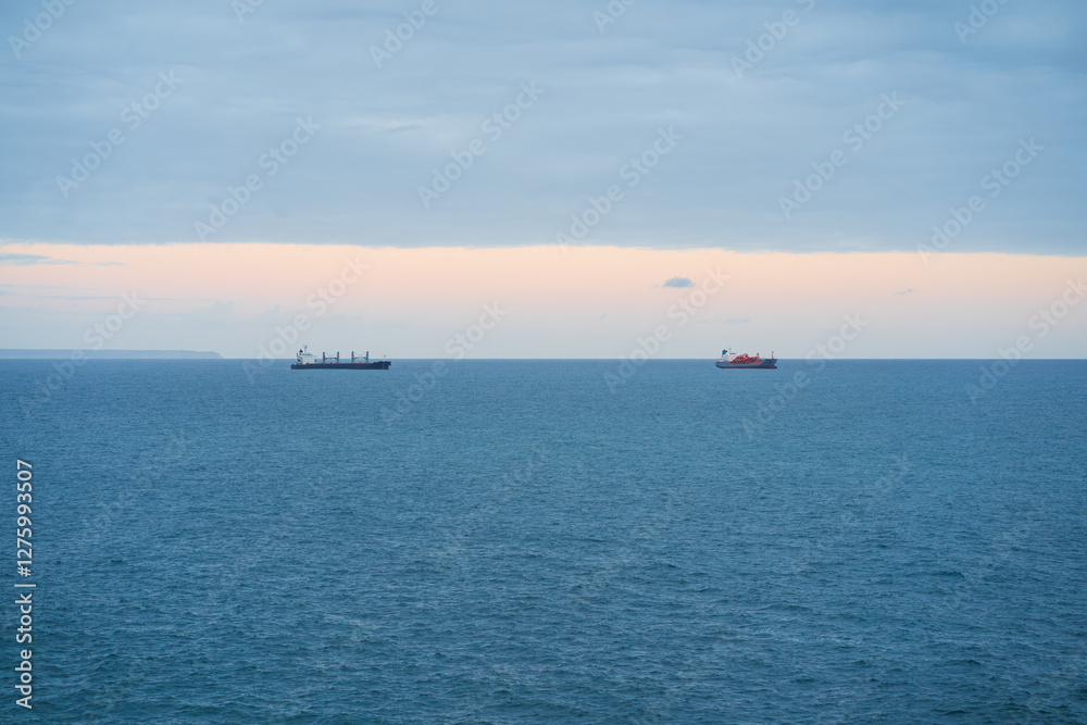 Two cargo ships on the horizon of the Atlantic Ocean, Portugal. Calm sea, cloudy sky with a glimpse of sunset. Two cargo ships on the horizon of the Atlantic Ocean, Portugal. Calm sea, cloudy sky with a glimpse of sunset.
