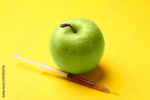 GMO concept. Green apple and syringe with liquid on yellow background, closeup