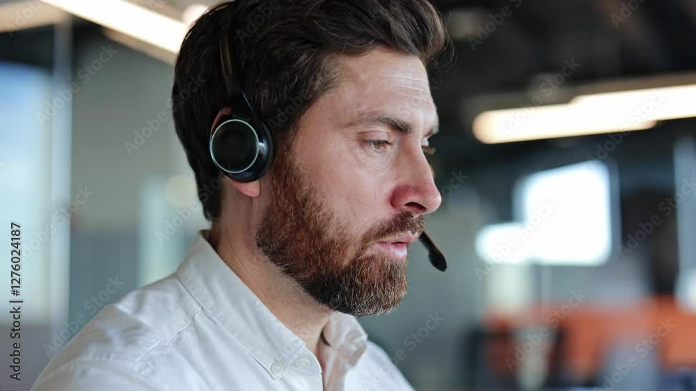 Focused businessman with headset assisting client in modern office. Bearded man providing professional customer service or tech support.
