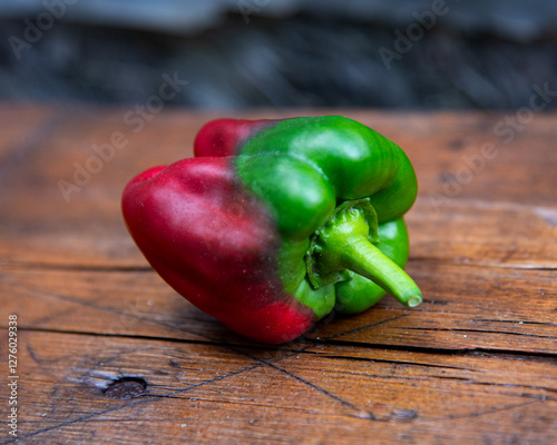 Double-colored paprika fruit on the wood surface, still life. Natural phenomenon. Bell pepper close up. Summer harvest, organic food planted at courtyard garden. Unique color pattern on vegetable. photo