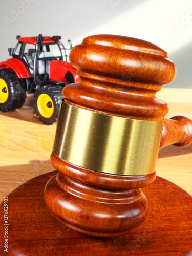 Agricultural vehicle auction concept: Closeup of a traditional wooden gavel on its block in close focus, with a defocused model tractor in the background.