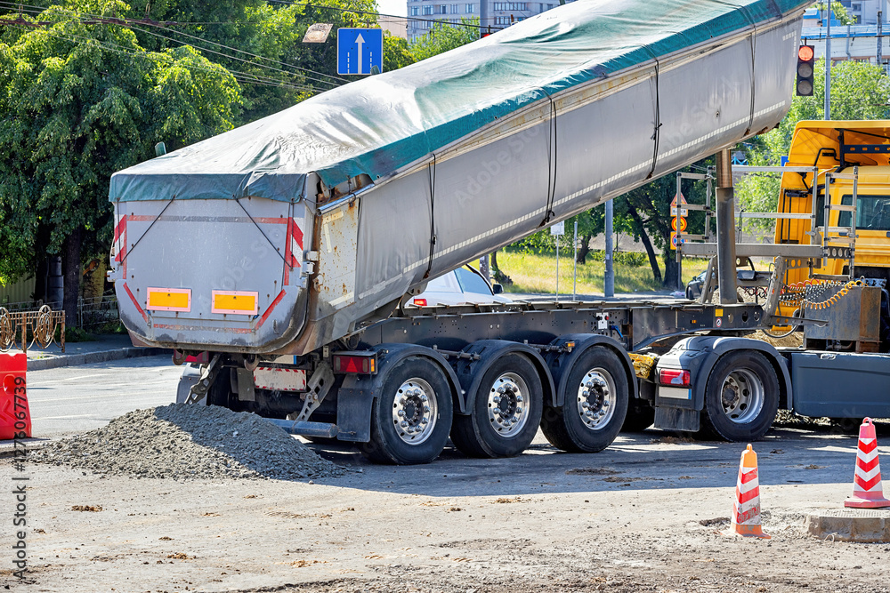 Construction activity showcases a truck unloading gravel at a busy intersection during the daylight. Copy space.