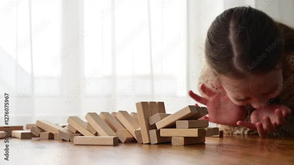 A girl plays Jenga with her mom, wooden blocks falling onto the table, capturing the fun and excitement of the game