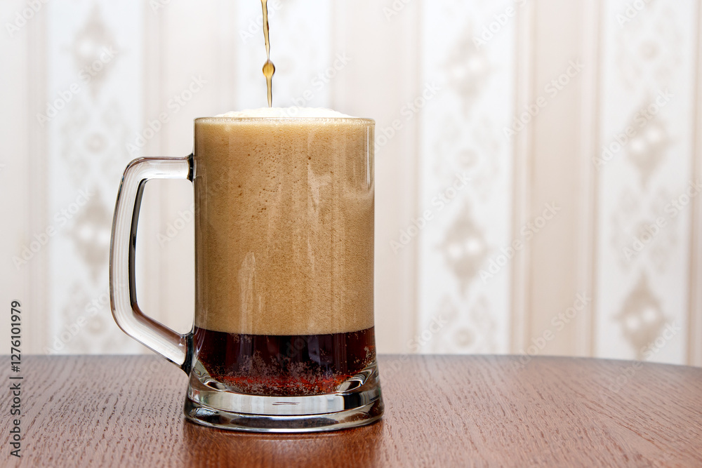 dark beer is poured into a glass mug