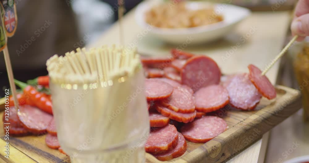Hand choosing salami slices with a toothpick from a charcuterie board, with breadsticks in the background. Perfect for culinary and appetizer concepts Hand choosing salami slices with a toothpick from a charcuterie board, with breadsticks in the background. Perfect for culinary and appetizer concepts