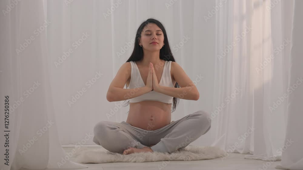Young happy Asian pregnant woman posing in studio with white curtains in background Young happy Asian pregnant woman posing in studio with white curtains in background