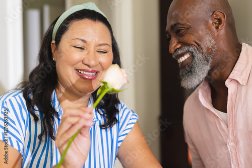 Smiling senior diverse couple enjoying rose together at home, celebrating special moment photo