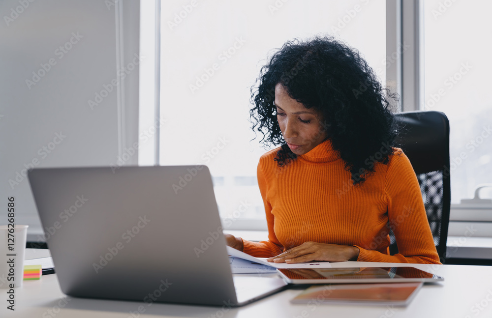 Dedicated digital nomad working in coworking space, reviewing documents while using laptop and tablet.She focuses on analyzing reports, demonstrating efficiency and remote work flexibility in office Dedicated digital nomad working in coworking space, reviewing documents while using laptop and tablet.She focuses on analyzing reports, demonstrating efficiency and remote work flexibility in office