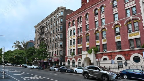 New York, United States, August 18, 2024. Street view in Harlem neighborhood. Old buildings overlook the street, cars. Pan motion.