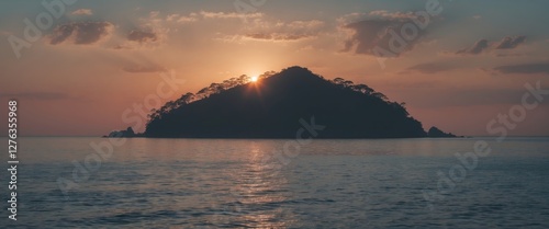 Sunset over tranquil waters with silhouette of a small island and cloudy sky in the background. photo