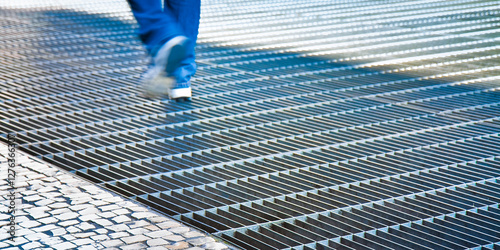 EAVY METAL GRATE PROTECTION PAVEMENT USED FOR VENTILATION OF UNDERGROUND SPACES - Ventilation iron grid on urban area with a person walking