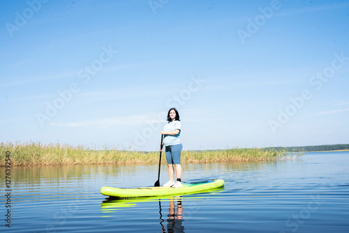  41 year old pregnant woman standing on stand up paddle board on river or lake on sunny summer day. Pregnancy after 40, traveling during pregnancy, active hiking and exercise in second trimester. photo