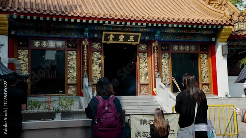 Praying in Chinese temple in Hong Kong, unrecognizable asian people pray with burning sticks. Confucian religion in China, local culture and traditions. Translation: saints and spirits united