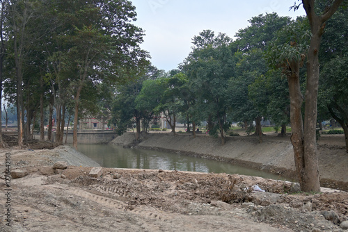 A serene landscape featuring a narrow, tranquil stream bordered by trees with lush green foliage.