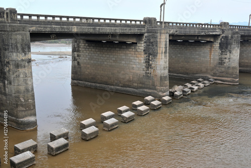 A concrete bridge spans across a muddy river, supported by large stone pillars.