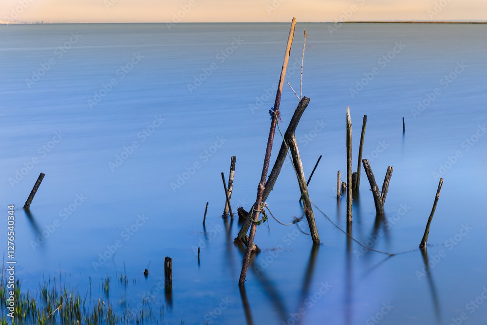 Fototapeta premium An old wooden fishing pier in Portugal in the area of Setubal at sunrise and low tide. Carrasqueira palafitic pier. A dilapidated fishing pier. Torso of a fishing pier.