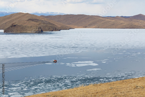 Beautiful landscape of a spring lake surrounded by picturesque mountains. A hovercraft transports tourists across Lake Baikal to Olkhon Island in the spring. photo