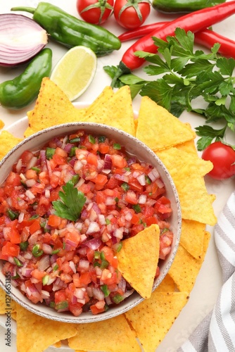 Delicious salsa in bowl, ingredients and nacho chips on beige table, flat lay