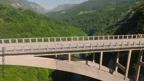 Aerial drone view of a woman walking on the high Djurdjevic Bridge, looking down at the Tara River and canyon in Montenegro