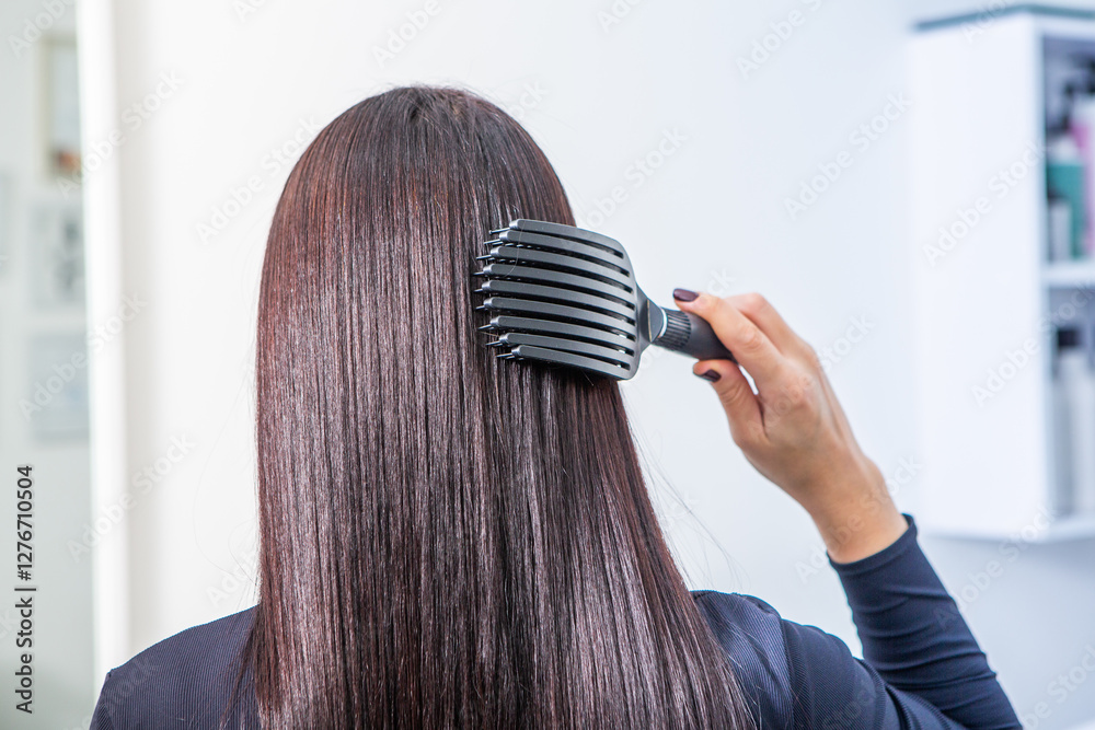 Naklejka premium woman combs her beautiful brunette hair at the beauty salon. Healthy hair