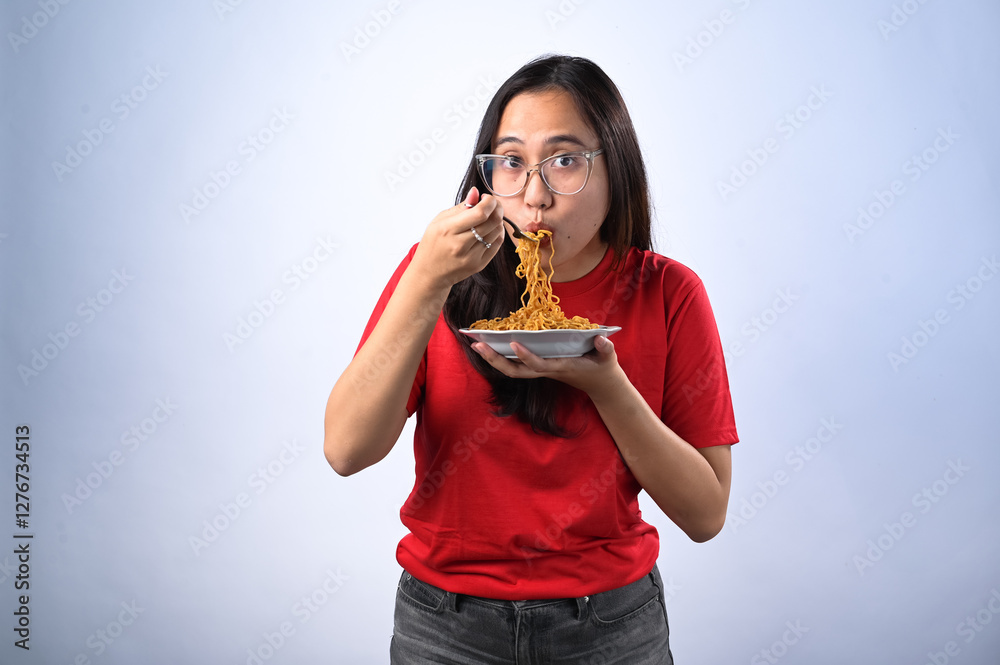 Asian woman in a red shirt and glasses enthusiastically eating instant noodles with a fork while giving a thumbs-up. She looks excited and satisfied. White background. Asian woman in a red shirt and glasses enthusiastically eating instant noodles with a fork while giving a thumbs-up. She looks excited and satisfied. White background.