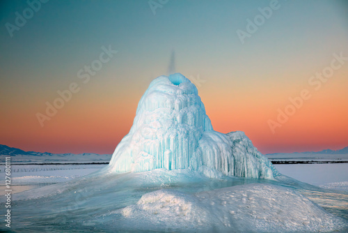 Frozen Water Geyser in Winter Landscape at Sunset
A striking natural ice formation created by a frozen water geyser rises from a snowy plain at sunset. 