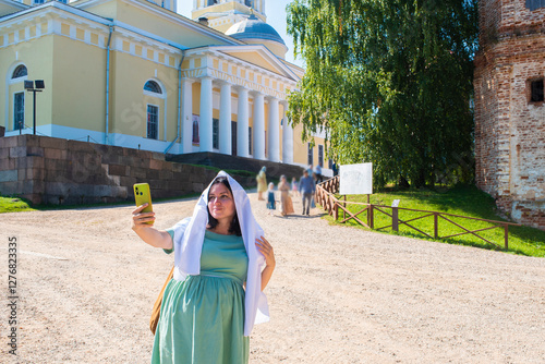 41 year old pregnant woman with a headscarf on her head takes a selfie on a smartphone against the backdrop of the Nilov Stolobenskaya desert, a monastery for men,. pregnancy after 40 photo