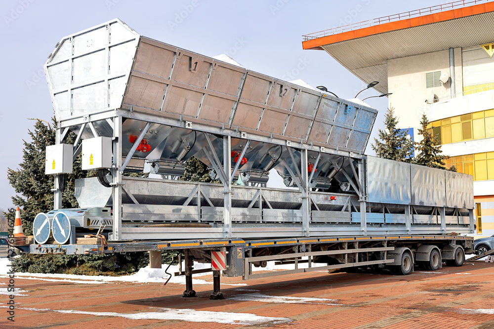 Large transport trailer with hoppers and red vibrators and shakers for ready-mix concrete mixing plants.
