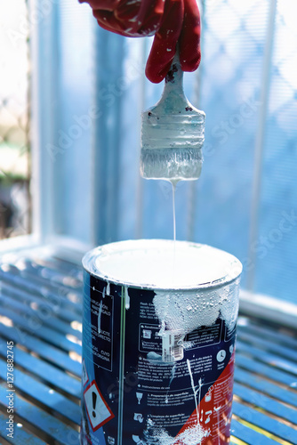 Latino worker of Mexican origin carrying out his work, painting a fence with white paint, happy, relaxed and dirty