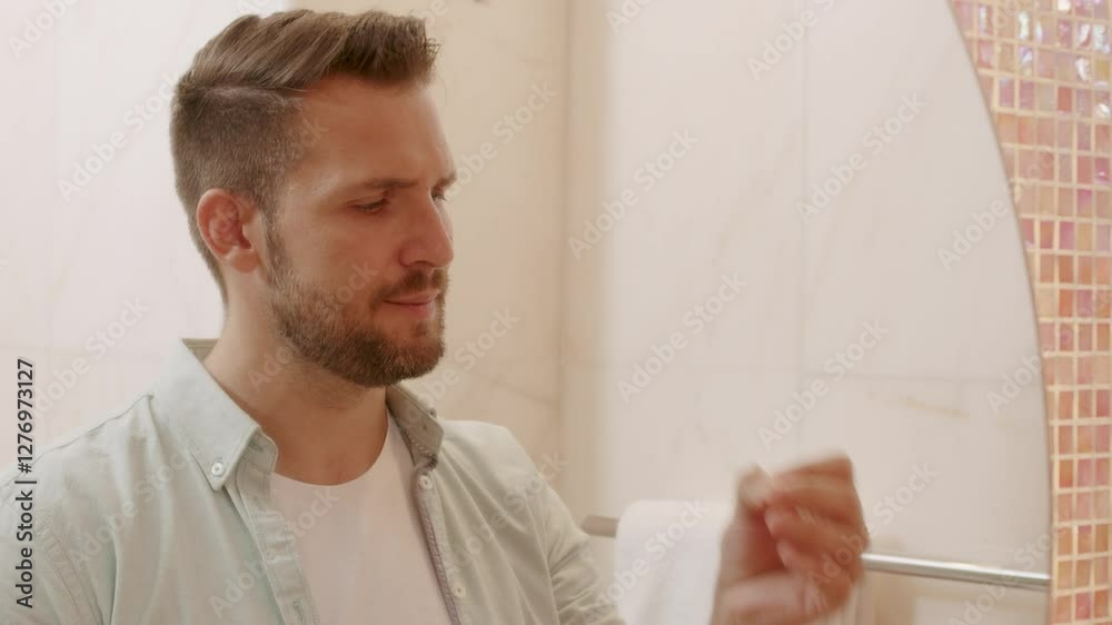 Smiling young man cleaning ear with cotton swab and looking to mirror at home bathroom Smiling young man cleaning ear with cotton swab and looking to mirror at home bathroom