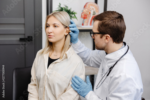 Otolaryngologist doctor checking young woman's ear using otoscope or auriscope at ENT clinic. Hearing exam