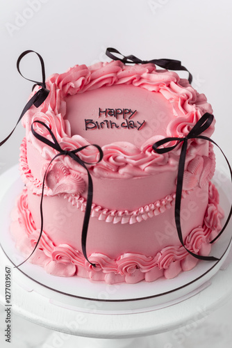 Delicate lambeth style birthday cake with pink cream cheese frosting decorated with cream tracery and happy birthday text on top. White background