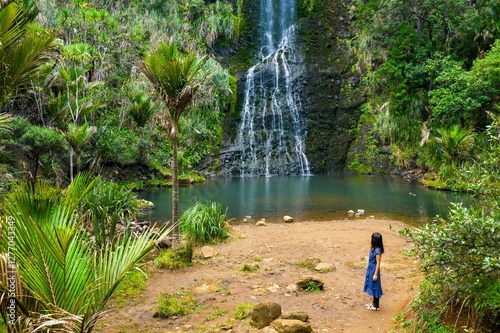 Woman observes a waterfall cascading into a tranquil pool, surrounded by lush tropical foliage. Nature's beauty. Karekare Falls, Karekare, Auckland, New Zealand photo