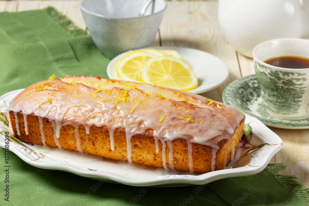 Aromatic lemon cake, covered with sugar icing and sprinkled with zest, served with tea.