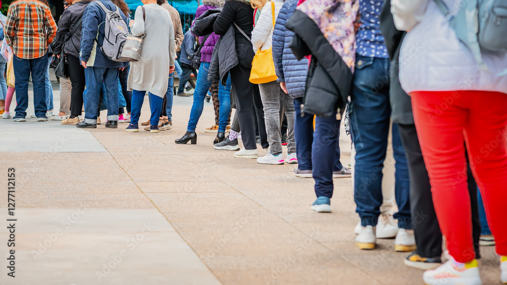 People standing in a long queue outdoors on city street. Public crowd. Women and men stand behind each other. Consumerism, waiting concept People standing in a long queue outdoors on city street. Public crowd. Women and men stand behind each other. Consumerism, waiting concept