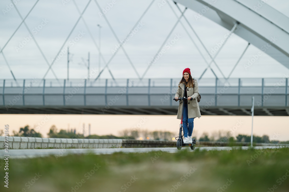 Woman Riding Electric Scooter Near Modern Bridge Outdoors Woman Riding Electric Scooter Near Modern Bridge Outdoors